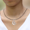 Black necklace with a silver moon pendant featuring a witch on a broomstick