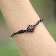 Black bracelet with a flower and a blue opal made of sawo...